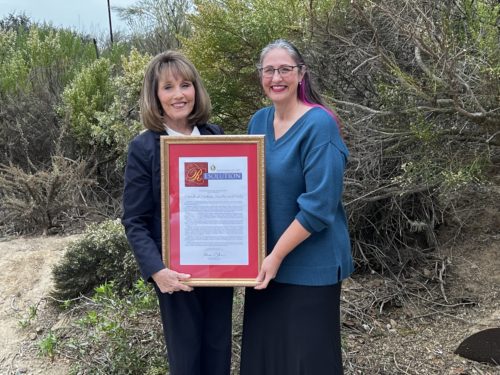 Two women hold a resolution standing against some bushes.